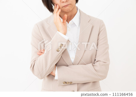 A middle-aged woman in a suit worries with her arms crossed 111166456