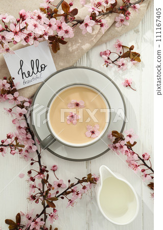 Spring twigs with flowers with a cup of hot drink, on a light wooden background. 111167405