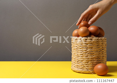 Eggs in a wicker basket, with a hand, on a gray background. 111167447