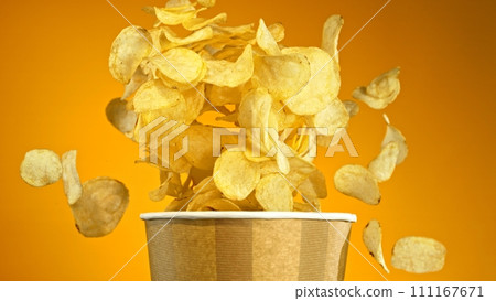 Flying Fried Potato Chips Exploding from Paper Bucket. Concept of Flying Junk Food. Flying Fried Potato Chips Exploding from Paper Bucket. Concept of Flying Junk Food. 111167671