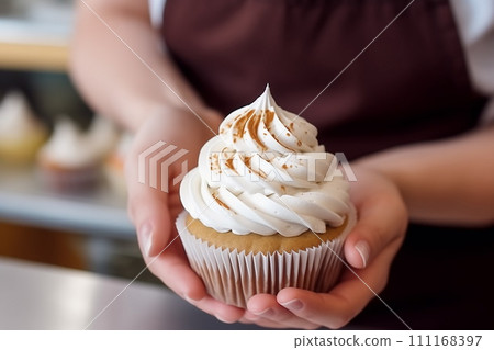 Closeup view of hands of female confectioner or baker holding fresh decorated cupcake with whipped cream top, AI Generative 111168397