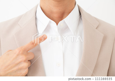 Middle-aged woman wearing a beige suit pointing at her collar 111169335