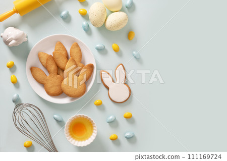 Preparation for Easter . Process cooking bunnies shaped cookies, ingredients, whisk and rolling pin on blue background. Space for text. View from above. Festive food and snacks. 111169724
