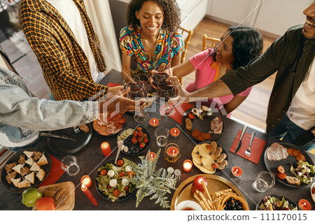 Group of happy friends is drinking wine and clinking glasses having holiday dinner party at home 111170015