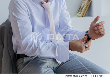 a man in a shirt puts a watch on his hand a man in a shirt puts a watch on his hand 111170399