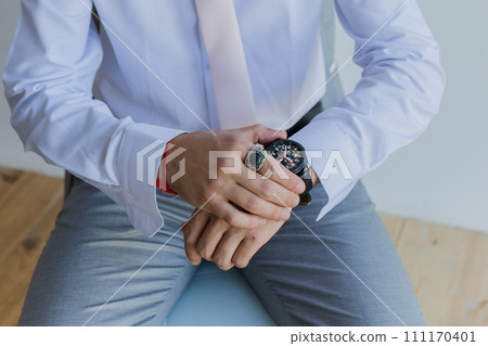 a man in a shirt puts a watch on his hand 111170401