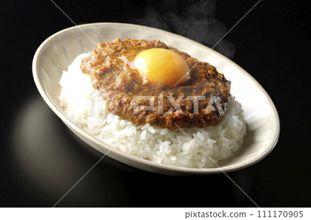 Hot keema curry topped with egg yolk photographed against a black background Hot keema curry topped with egg yolk photographed against a black background 111170905