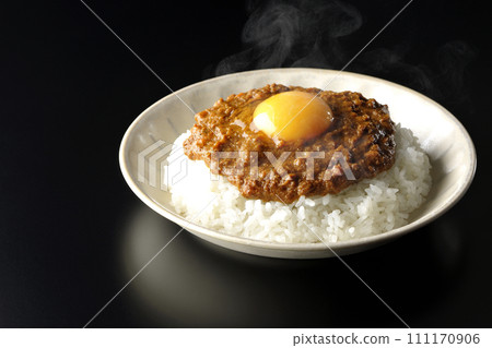 Hot keema curry topped with egg yolk photographed against a black background 111170906