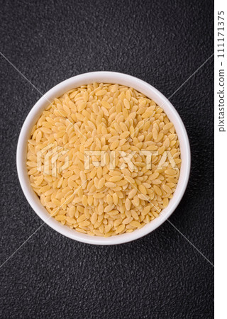 Raw risoni pasta made from durum wheat on a dark concrete background Raw risoni pasta made from durum wheat on a dark concrete background 111171375