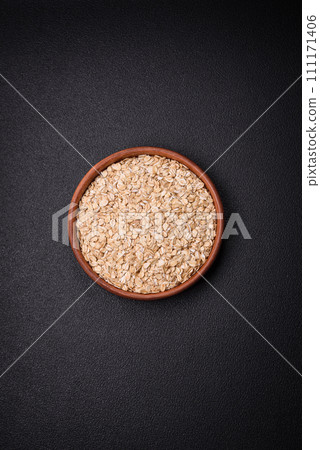 Raw oatmeal flakes in a ceramic bowl on a dark concrete background 111171406