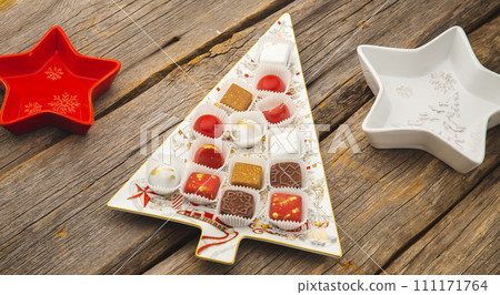 Chocolates in a red festive box dark chocolate truffle on a Christmas background with New Year's toys balls fir branches. flat mock up copy space. 111171764