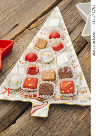 Chocolates in a red festive box dark chocolate truffle on a Christmas background with New Year's toys balls fir branches. flat mock up copy space. 111171765