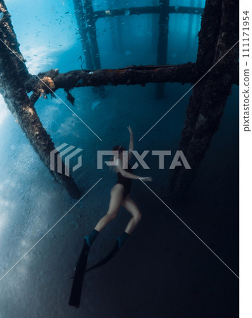 Woman free diver swims underwater on deep in transparent ocean. Freediving under the pier 111171954
