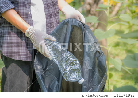 Hand holding plastic bottle waste, picking up trash putting to the black garbage bag at Sunflower Park on Environmental Earth day 111171982