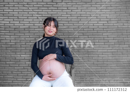 Mom pregnant woman in a dress holds hands on belly on black brick background, Waiting for the birth of your baby with love 111172312