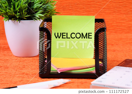 Business Concept. Welcome text written on a green sticker next to office supplies on an orange background Business Concept. Welcome text written on a green sticker next to office supplies on an orange background 111172527