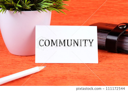 The word Community written on a business card next to a business card holder, a green flower and a pencil on an orange background 111172544