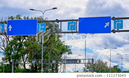 Blue pointing empty road signs with arrows and cloudy sky and trees 111173043
