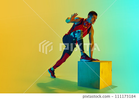 Athlete in sportswear training, doing exercises with wooden box against gradient blue yellow background in neon light Athlete in sportswear training, doing exercises with wooden box against gradient blue yellow background in neon light 111173184