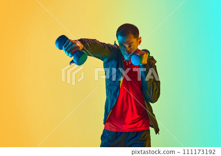Hand exercises. Athletic man in sportswear training with dumbbells against gradient blue yellow background in neon light 111173192