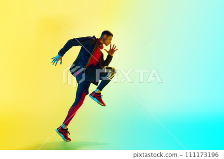Dynamic image of young athletic man in sportswear, training, running against gradient blue yellow background in neon light 111173196