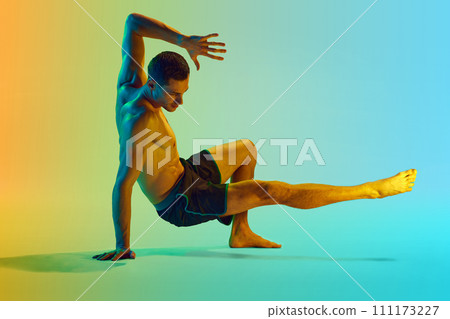 Young shirtless man with muscular, relief, strong body training, doing workout exercises against gradient blue yellow background in neon light Young shirtless man with muscular, relief, strong body training, doing workout exercises against gradient blue yellow background in neon light 111173227