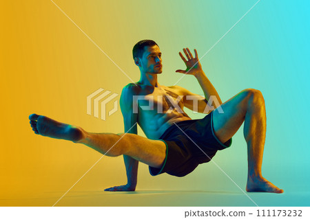 Intensive full-body training. Muscular athletic young shirtless man, with fit body doing workout exercises against gradient blue yellow background in neon light Intensive full-body training. Muscular athletic young shirtless man, with fit body doing workout exercises against gradient blue yellow background in neon light 111173232