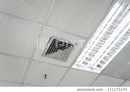 Ceiling mounted cassette type air conditioner and modern lamp light on white ceiling. Duct air conditioner for home, hall or office. Ceiling mounted cassette type air conditioner and modern lamp light on white ceiling. Duct air conditioner for home, hall or office. 111175274