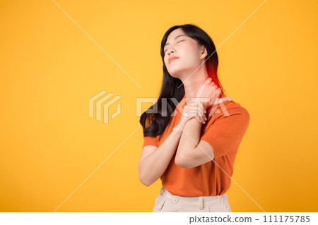 Supportive Asian woman in her 30s, wearing an orange shirt, holds her painful neck on yellow background. office syndrome health care concept. 111175785
