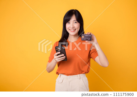 Enthusiastic young Asian woman in her 30s, using smartphone and holding credit card on yellow background. Swift online shopping. 111175900