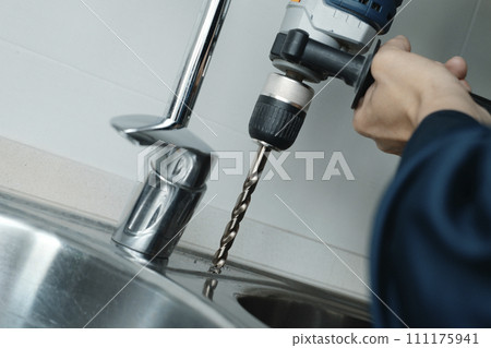 man drilling a hole in a kitchen sink 111175941
