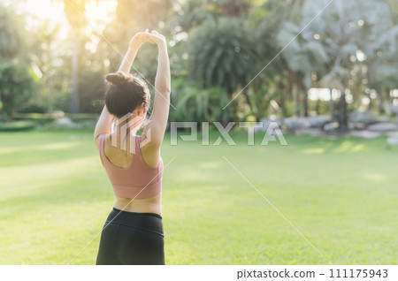Back portrait of a 30s Asian woman, wearing pink sportswear, preparing her body and breathing fresh air before a sunset run in a public park. Embrace a wellness lifestyle and fitness outside. 111175943