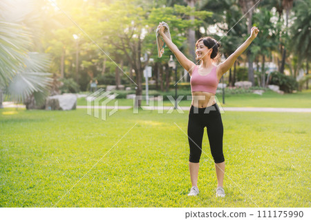 Experience the wellness of a happy fit female jogger. Asian woman in her 30s wearing pink sportswear, breathing fresh air in a public park. Embrace a nature-inspired wellness living concept 111175990