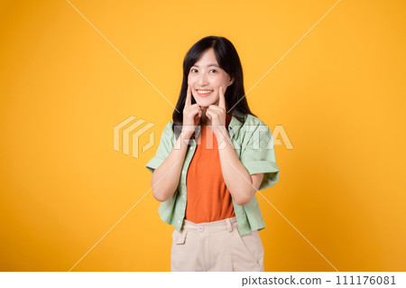 Young asian woman in her 30s wearing orange shirt and green jumper pointing to her teeth isolated on yellow background. dental healthcare concept. Young asian woman in her 30s wearing orange shirt and green jumper pointing to her teeth isolated on yellow background. dental healthcare concept. 111176081