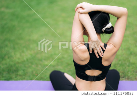 portrait fit young 30s Asian woman in pink sportswear with yoga mat. stretching arm muscles in park. Embrace active lifestyle with outdoor fitness. A dedicated athlete finds serenity in nature beauty. 111176082