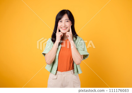 dental care with young Asian woman 30s, dressed in orange shirt and green jumper points to her teeth, isolated on a vibrant yellow background, highlighting the importance of dental healthcare dental care with young Asian woman 30s, dressed in orange shirt and green jumper points to her teeth, isolated on a vibrant yellow background, highlighting the importance of dental healthcare 111176083