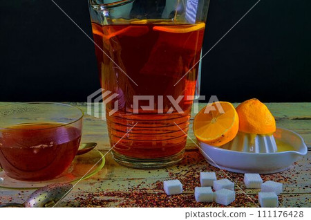Black tea, a cup of black tea, manual squeezer with lemons. A jug of black tea and cubes of sugar. Dark image Black tea, a cup of black tea, manual squeezer with lemons. A jug of black tea and cubes of sugar. Dark image 111176428