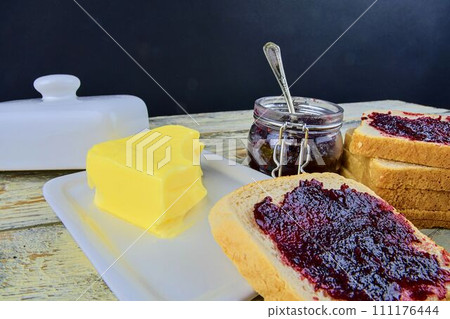 Jam, butter in butter dish and jam spread on toast. Healthy and diet concept. Rural white wooden background. Jam, butter in butter dish and jam spread on toast. Healthy and diet concept. Rural white wooden background. 111176444