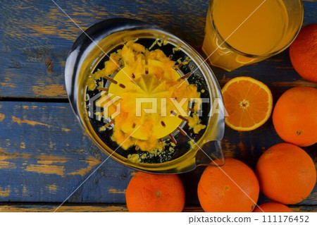 Tangerines, oranges, a glass of orange juice and manual citrus squezeer on blue wooden background. Oranges cut in half. Top view, flat design Tangerines, oranges, a glass of orange juice and manual citrus squezeer on blue wooden background. Oranges cut in half. Top view, flat design 111176452
