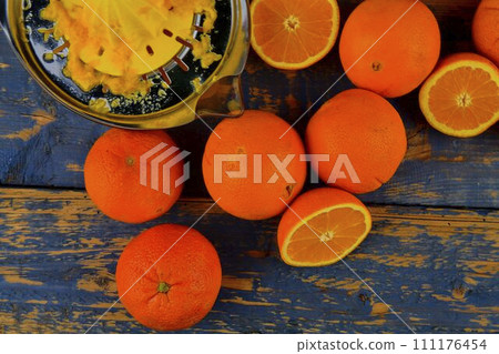Tangerines, oranges, a glass of orange juice and manual citrus squezeer on blue wooden background. Oranges cut in half. Top view, flat design Tangerines, oranges, a glass of orange juice and manual citrus squezeer on blue wooden background. Oranges cut in half. Top view, flat design 111176454