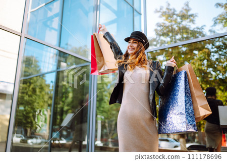 Stylish woman with shopping bags walks through the city streets. Spring Style. 111178696