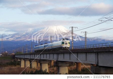 The reprinted green-colored 381 series limited express Yakumo runs over the long railway bridge of the Hino River with the snow-capped Mt. Mt. in the background. The reprinted green-colored 381 series limited express Yakumo runs over the long railway bridge of the Hino River with the snow-capped Mt. Mt. in the background. 111178765