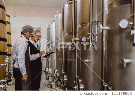 Winemaker professional working in modern large winery factory liquor alcohol drinks industry quality control and fermentation monitor vintage color tone 111179060