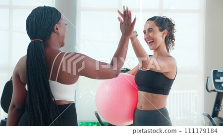 Two young woman in sportswear workout routines using exercise ball in fitness gym. Two young woman in sportswear workout routines using exercise ball in fitness gym. 111179184