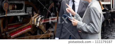 Young caucasian engineer man and woman in suit checking train with tablet in station. Young caucasian engineer man and woman in suit checking train with tablet in station. 111179187