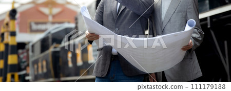 Young caucasian engineer man and woman in suit checking train looking blueprint in station. Young caucasian engineer man and woman in suit checking train looking blueprint in station. 111179188
