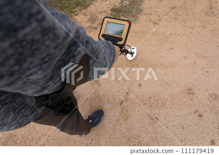 Cropped Man Holds Waterproof Metal Gold Detector, White Coil Above Ground. Excavation, Search for Treasure Or Ancient Things. Archeology, Minesweeper. Horizontal Nobody 111179419