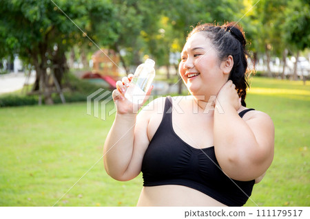 Active plus size woman hydration drinking a water bottle outdoors. 111179517