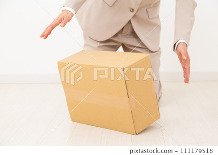 A middle-aged woman in a suit panics after dropping a cardboard box. 111179518
