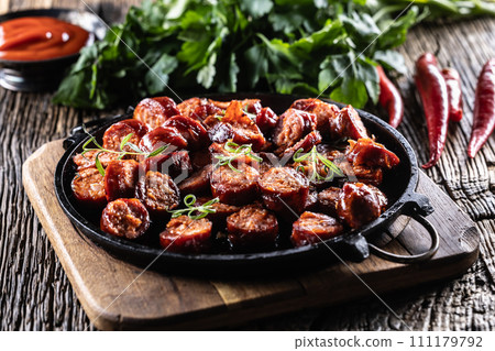 Sliced sausages fried with spices, bbq sauce and herbs - close up 111179792